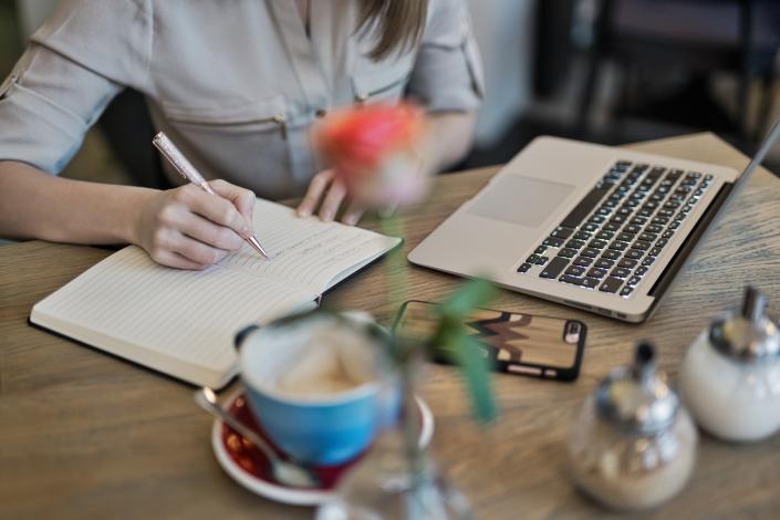 Person writing in a notebook next to laptop