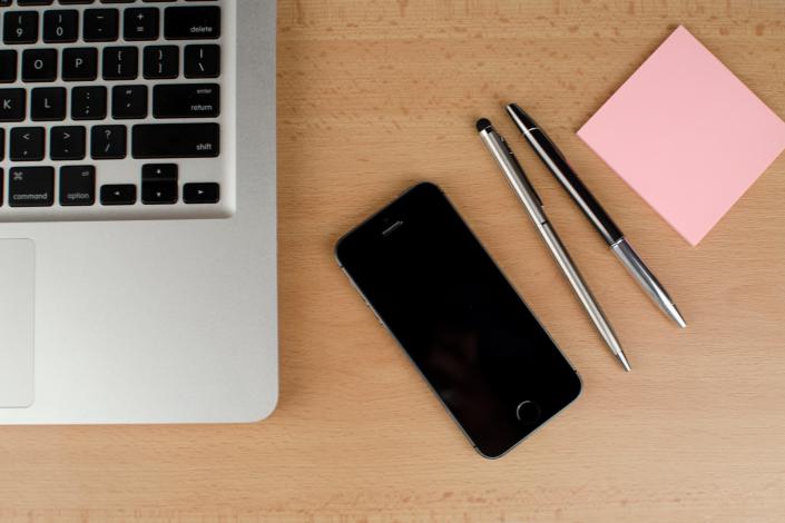 Image of laptop, cellphone, pens, and notepad on a desk