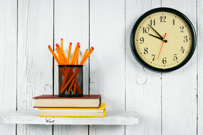  box of pencils sitting on top of two books with a clock behind it