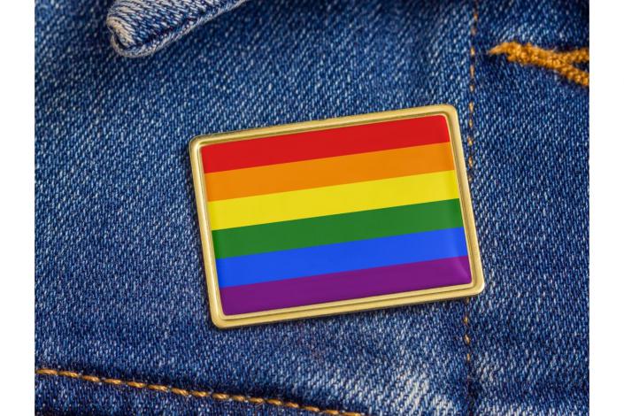 rainbow flag pin attached to the collar of a jean jacket 