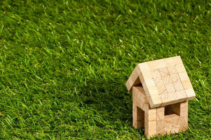 small wooden block house in bottom right corner on a field of grass